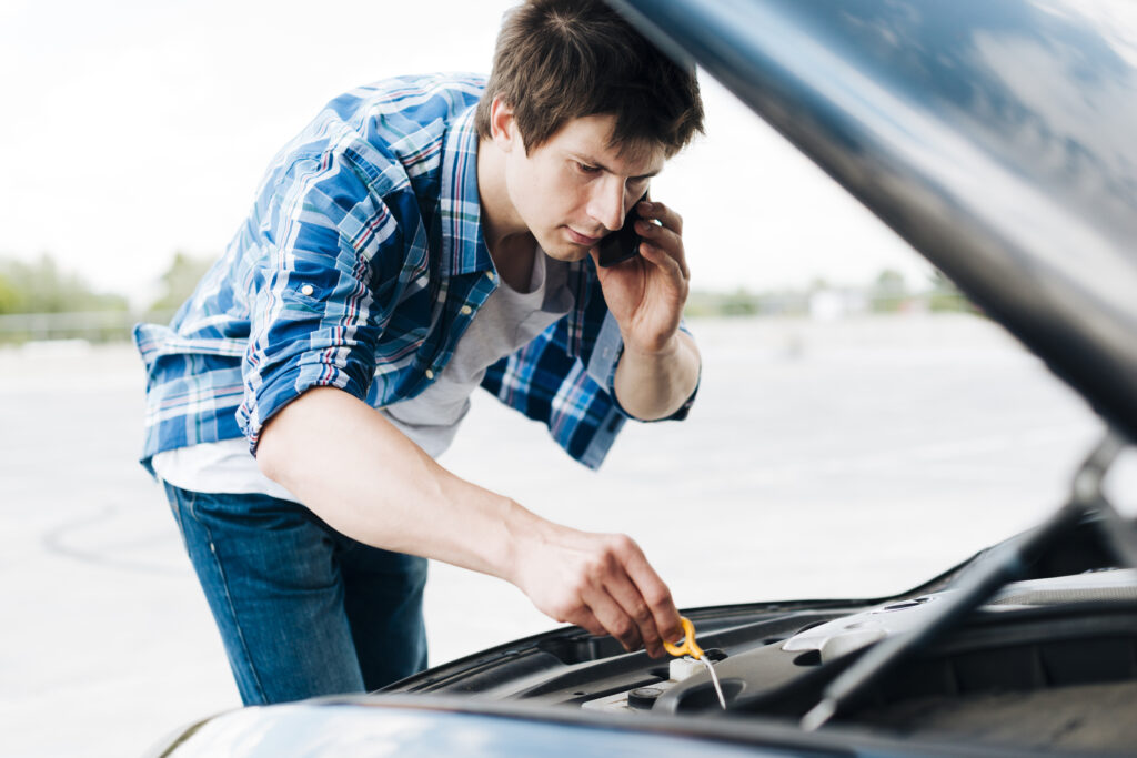 man checking oil talking phone