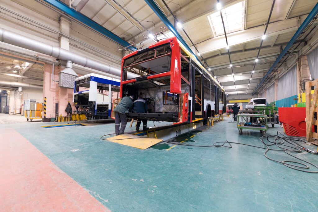 One working day of modern automatic bus manufacturing with unfinished cars workers in protective uniform automotive parts.
